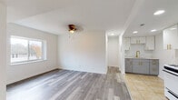 Located at 320 Grafton Ave in Dayton, Ohio, this thoughtfully updated single-floor home offers a clean, modern aesthetic throughout. The open living and dining area is finished with durable grey-toned laminate hardwood flooring and crisp white walls, creating a bright and welcoming atmosphere. A ceiling fan provides comfort, while a well-placed window allows natural light and outdoor views to fill the space. The layout flows seamlessly into the kitchen, which features glossy white cabinetry with gold hardware, tile flooring, a gas range, stainless steel over-the-range microwave, and a refrigerator — offering both style and function. The bedrooms are generously sized, each with the same grey laminate flooring, neutral white walls, and large windows that bring in ample natural light and views of the surrounding neighborhood. The bathrooms are finished to a consistent, elevated standard, with grey vanities topped by marble-look countertops, tub-shower combinations, and cohesive gold fixtures and hardware throughout — lending a polished, contemporary feel. Additional details include visible HVAC vents and a welcoming entryway with a paneled door. The overall design is clean, cohesive, and move-in ready.