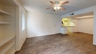 This single-story residence offers a well-organized layout with distinct living, sleeping, and functional zones. The main living area features wood-look hard flooring, a ceiling fan with light fixture, a textured ceiling, and built-in shelving along one wall. A sliding glass door with vertical blinds opens to an outdoor patio, allowing natural light to fill the space. The living area connects openly to the kitchen, which is equipped with white cabinetry, dark laminate countertops, a double sink, electric range, built-in microwave, refrigerator, and a skylight panel overhead for additional brightness.

A secondary carpeted room, accessible from the main living area, also features a ceiling fan, sliding glass door with patio access, and a textured ceiling. The walk-in closet offers wall-mounted hanging rods on multiple sides and a central shelving unit, providing ample storage capacity. The bathroom includes a vanity with dark countertops, under-sink cabinetry, a mirrored medicine cabinet, and a full tub-shower combination. Wood-look flooring extends throughout the non-carpeted areas, providing a cohesive aesthetic across the unit.