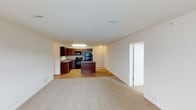 This single-floor, two-bedroom, one-bathroom residence offers a practical and well-organized layout designed for comfortable everyday living. The open-concept design seamlessly connects the living area and kitchen, creating a cohesive and airy feel throughout the main living space.

The kitchen is outfitted with rich dark wood cabinetry, granite-look countertops, and a full suite of black appliances, including a refrigerator, range, and microwave. A kitchen island provides additional prep and dining space, while hardwood-style flooring anchors the cooking and dining zone with a warm, polished look.

The adjoining living area features neutral wall-to-wall carpeting, offering a soft and comfortable surface underfoot. The open flow between these two areas makes the space feel expansive and inviting. Recessed and flush-mount ceiling lighting provides consistent illumination throughout.

A closet adjacent to the living area offers convenient built-in storage. The clean, neutral color palette — featuring crisp white walls and ceilings — lends the home a bright, move-in-ready aesthetic that is easy to personalize. The thoughtful layout and functional finishes make this residence well-suited for a variety of living arrangements.