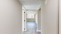 This 2-bedroom, 1-bathroom residence offers a thoughtfully designed single-story layout that makes efficient use of its space. Consistent light wood-tone laminate flooring flows throughout the unit, creating visual continuity across all rooms.

The combined kitchen and living area forms the heart of the unit. The kitchen features tall white cabinetry extending to the ceiling, stainless steel appliances including a refrigerator, range, and microwave, and a striking marble-look quartz peninsula countertop that serves as a natural divider between the kitchen and living space. The living area benefits from natural light streaming through vertical-blind-covered windows with urban exterior views.

Both bedrooms are comfortably sized with neutral beige walls, the same wood-tone flooring, and windows fitted with vertical blinds offering city views. The primary bedroom provides a generous footprint. A dedicated hallway with a closet connects the rooms efficiently.

The bathroom is finished with large-format marble-look tile on both the floors and shower walls, complemented by a soaking tub and clean white trim, lending a polished, contemporary feel to the space.