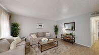 This single-story, 2-bedroom, 1-bathroom home offers a practical and comfortable layout across a compact yet efficiently organized floor plan. The living room serves as the heart of the home, featuring light wood-style flooring, neutral gray walls, and a textured ceiling. Large windows dressed with layered curtains allow natural light to fill the space, creating a bright and welcoming atmosphere.

Adjacent to the living area, the dining room provides an intimate space for meals, with a window that brings in additional natural light. The kitchen is well-equipped, featuring white cabinetry, marble-style countertops, a full suite of white appliances including a range, microwave, and dishwasher, all set atop matching wood-style flooring.

Both bedrooms are carpeted for comfort and each features a ceiling fan with light fixture, windows with curtain panels, and dedicated closet space. The primary bedroom is generously proportioned, offering ample room for a full furniture arrangement.

The single bathroom includes a vanity with a light countertop, tile wainscoting along the walls, and a large mirror. A hallway connects the main living areas to the bedrooms and bathroom, providing a logical and functional flow throughout the home.