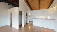 Located at 1815 North Hutchinson Road in Spokane, Washington, Unit 61 is a single-floor residence defined by its striking architectural character. The most prominent feature is the soaring vaulted ceiling with warm, natural wood planking and bold exposed dark beams that run the length of the living area, creating a sense of openness and rustic charm throughout the space.

The living area is bright and airy, with light wood laminate flooring that complements the ceiling's natural tones. A stone-surround wood-burning fireplace anchors one wall, while a sliding glass door opens to an outdoor patio area, allowing natural light to flood the interior and providing a seamless connection to the outdoors. A wall-mounted A/C unit and baseboard heating ensure year-round comfort.

The kitchen area features white cabinetry, a countertop with a sink, and includes a full-size refrigerator and range. The kitchen is finished with tile flooring and benefits from the same exposed beam ceiling detail. A peninsula counter separates the kitchen from the living space, which also showcases white vertical shiplap-style wall paneling for added texture.

The unit includes a closet with built-in shelving for storage, a dedicated water heater closet, and a full bathroom finished with tile flooring, a tub/shower combination, a vanity with a granite-style countertop, and a mirror with built-in storage.