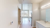 Located at 3609 Wynkoop St in Denver's vibrant River North Art District, this modern single-floor unit combines contemporary design with urban industrial character. Light wood flooring flows throughout the open living area, which is bathed in natural light from large windows offering city views. An exposed metallic duct runs overhead, lending an industrial loft aesthetic that complements the clean, white walls and high ceilings.

The kitchen is efficiently designed and fully equipped with stainless steel appliances, including a refrigerator, electric range, over-the-range microwave, and dishwasher. White cabinetry and open wood-bracket shelving provide practical storage, while the white countertops and stainless steel sink complete the modern look.

The bathroom features light large-format tile flooring, a walk-in shower with white subway tile surround, grab bars, a toilet, and a separate vanity area with a white undermount sink, ample cabinet storage, and a well-lit mirror. The entry is highlighted by a distinctive wood-paneled door with a bold blue frame, adding a striking design detail. Track lighting and climate control systems are integrated throughout, ensuring comfort and functionality in this thoughtfully designed Denver residence.