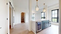 This thoughtfully designed 2-bedroom, 3-bathroom residence spans a single floor and offers a refined blend of modern aesthetics and functional living. Light hardwood flooring flows through the open-concept living, dining, and kitchen areas, anchored by floor-to-ceiling black-framed windows that flood the space with natural light and frame expansive outdoor views.

The kitchen is a standout, featuring two-toned cabinetry in white and slate blue, striking quartz countertops, gold hardware, a beverage refrigerator, and a full suite of stainless steel appliances. A large island with a waterfall edge provides additional prep and seating space. Pendant lights with brass accents add a warm, contemporary touch. The living and dining area continues the bright, airy feel with a bold gold chandelier and unobstructed panoramic views.

The generously sized primary bedroom opens to a private balcony through black-framed glass doors, offering serene views. It includes a well-appointed walk-in closet with built-in shelving. The second bedroom features plush carpeting, a large window, and convenient access to additional closet space. The bathrooms are finished with clean white cabinetry, quartz surfaces, and polished gold fixtures, including a soaking tub with tiled surround. A connecting hallway ties all spaces together cohesively.