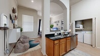 This single-floor, 2-bedroom, 2-bathroom residence offers a thoughtfully designed layout that balances open communal spaces with comfortable private retreats. The kitchen serves as a central hub, featuring warm wood cabinetry with abundant storage, dark granite countertops, stainless steel appliances including a range, microwave, and refrigerator, and a peninsula island with a sink that opens toward the living area via an elegant arched pass-through. An in-unit washer and dryer closet is conveniently located just off the kitchen. The living room is bright and airy, benefiting from tall ceilings, large windows, a transom window above the exterior door, and light wood-style flooring throughout. Both bedrooms are carpeted and generously sized, each with natural light from windows. The primary bedroom is notably spacious and is accompanied by a dual-sink bathroom with granite countertops and a long vanity. A large walk-in closet with multi-level wire shelving provides ample storage. The second bathroom features a single vanity with granite countertops, overhead cabinetry, and a shower-tub combination. A dedicated hallway and closet round out the functional layout of this well-organized residence.