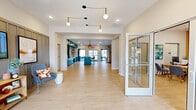 Located at 101 Lemon Dr in Lake Saint Louis, MO, this thoughtfully designed single-floor community space offers a generous, open layout that seamlessly connects key gathering areas. The entrance greets visitors with light wood flooring, an eye-catching sculptural pendant light fixture, and a welcoming seating nook accented by a board-and-batten feature wall with a mounted display screen and curated shelving.

The open-concept interior flows through a wide hallway into the combined living, dining, and kitchen area. The living room centers around a striking floor-to-ceiling stacked stone fireplace, complemented by warm leather seating and abundant natural light from large windows. Adjacent to this, the dining area features a statement live-edge wood table surrounded by mustard-yellow chairs beneath oversized drum pendant lights, with botanical artwork adorning the crisp white walls.

The kitchen is a standout, showcasing bold teal cabinetry, a textured brick backsplash, and an expansive white quartz island with bar seating. Woven gold pendant lights add warmth overhead, while glass doors open directly to an outdoor patio. Stainless steel appliances and ample storage complete this highly functional and visually striking space. Light wood flooring ties the entire interior together, creating a cohesive, modern, and inviting atmosphere throughout.