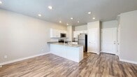 Located on W Grassland Dr in Lehi, Utah, this two-story home offers three bedrooms, three bathrooms, and a thoughtfully designed layout spread across two levels. The upper floor comprises the majority of the living space, while the lower level houses a two-car garage accessible via a staircase.

The kitchen is a standout feature, showcasing white shaker-style cabinetry, gray quartz-style countertops, stainless steel appliances including a refrigerator, electric range, and microwave, and a peninsula with a built-in sink. Wood-look luxury vinyl plank flooring runs throughout the kitchen and main living areas, lending warmth and durability to the space.

The three bedrooms are carpeted and finished in neutral tones, each with windows that allow natural light to filter in. The primary bedroom offers generous proportions and dedicated closet space. Sliding double closet doors are featured in one of the secondary bedrooms, providing ample storage.

All three bathrooms are finished with tile flooring and gray countertops. One bathroom features a full tub-shower combo, while another is configured as a more compact water closet with a frosted window for privacy.

A dedicated laundry room with tile flooring and washer/dryer hookups adds everyday convenience. Five closets throughout the home provide abundant storage. The overall aesthetic is clean, modern, and move-in ready.
