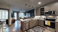 This single-floor residence is designed with a contemporary aesthetic, combining functionality and style across its open layout. The kitchen serves as a central hub, outfitted with gray shaker-style cabinetry, granite countertops, a subway tile backsplash, and a full suite of stainless steel appliances including a dishwasher, range, and over-the-range microwave. A peninsula with seating for multiple bar stools extends the counter space and creates a natural transition into the living area. A trio of sleek black pendant lights hang above, adding a modern design element. Wood-look flooring runs throughout the main living spaces, complementing the open-concept flow.

The living room features a bold teal accent wall, large windows that allow ample natural light, and generous space for comfortable seating arrangements. Two bedrooms offer carpeted flooring, multiple windows with blinds, and room for substantial furniture. The full bathroom is finished with large-format tile surrounding a soaking tub-shower combination, a granite vanity, and direct access to a dedicated walk-in closet with built-in shelving and hanging rods—adding practical storage to the residence.