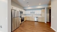 This single-story, 3-bedroom, 1-bathroom home offers a thoughtfully designed layout across a comfortable footprint. Warm wood-look flooring runs throughout, complementing the neutral, light-toned walls that give the space a clean and modern feel.

The open-concept kitchen and living area serves as the heart of the home. The well-equipped kitchen features a dual-tone cabinet design — white upper shaker cabinets paired with natural light wood lower cabinets — topped with white countertops. A full suite of stainless steel appliances includes a refrigerator, electric range, microwave, and dishwasher. Recessed lighting adds brightness to the space.

The living area is generously sized with a sliding glass door that invites natural light and provides views of the outdoors. Three bedrooms offer comfortable personal spaces, with the primary bedroom providing a spacious retreat. Each room benefits from the consistent flooring and neutral palette found throughout the home.

The bathroom includes a full walk-in shower with clean white surround and built-in shelving nearby for convenient storage. A dedicated laundry room houses a full-size washer and dryer, adding to the home's practical amenities. Three closets provide ample storage throughout the residence, completing a functional and move-in-ready living space.