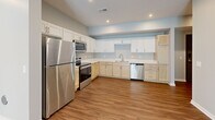 This single-story, 3-bedroom, 1-bathroom home offers a thoughtfully designed layout across a comfortable footprint. Warm wood-look flooring runs throughout, complementing the neutral, light-toned walls that give the space a clean and modern feel.

The open-concept kitchen and living area serves as the heart of the home. The well-equipped kitchen features a dual-tone cabinet design — white upper shaker cabinets paired with natural light wood lower cabinets — topped with white countertops. A full suite of stainless steel appliances includes a refrigerator, electric range, microwave, and dishwasher. Recessed lighting adds brightness to the space.

The living area is generously sized with a sliding glass door that invites natural light and provides views of the outdoors. Three bedrooms offer comfortable personal spaces, with the primary bedroom providing a spacious retreat. Each room benefits from the consistent flooring and neutral palette found throughout the home.

The bathroom includes a full walk-in shower with clean white surround and built-in shelving nearby for convenient storage. A dedicated laundry room houses a full-size washer and dryer, adding to the home's practical amenities. Three closets provide ample storage throughout the residence, completing a functional and move-in-ready living space.