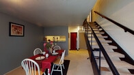 Located in the Quad area of Carbondale, IL, this two-story residence offers a well-organized layout across two floors connected by a carpeted staircase with a metal railing. The main level features a comfortable living room with exposed painted cinder block walls, carpet flooring, and a large window that allows natural light to fill the space. A dedicated dining area sits adjacent to the kitchen, providing room for a full dining table and seating. The kitchen is equipped with a coil-burner electric range, ample white cabinetry, and a pass-through window that opens to the living and dining areas, enhancing the open feel of the main floor. The entry area includes a coat closet and access to a full bathroom featuring a vanity, toilet, and a tub-shower combination. The upper floor houses multiple bedrooms, each carpeted and featuring painted cinder block accent walls, windows with natural views of surrounding greenery, and sufficient space for bedroom and study furniture. The textured ceilings are consistent throughout the residence, and the overall layout provides clearly defined living, dining, and sleeping zones across both levels.