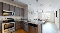 Located at 113-121 N 20th St in Richmond, VA, this two-bedroom, one-bathroom unit offers a well-designed single-level layout that maximizes functionality across a compact yet comfortable footprint. The open-concept living and kitchen area forms the heart of the unit, where light hardwood-style flooring runs throughout. The kitchen is outfitted with rich dark cabinetry, granite countertops, a full suite of stainless steel appliances including a refrigerator, range, and microwave, and a peninsula with bar seating — ideal for casual dining or entertaining. Pendant and track lighting add a polished touch overhead. The living room is bright and airy, featuring a ceiling fan, clean white walls, and a window that allows natural light to fill the space. Both bedrooms are carpeted and offer a calm, neutral palette. The primary bedroom provides a comfortable amount of space, while both rooms are served by a shared full bathroom featuring a granite-topped vanity with an undermount sink and matching cabinetry. A dedicated closet with built-in shelving provides additional storage. The unit also includes an in-unit laundry area with a full-size washer and dryer hookup, adding everyday convenience to this well-appointed Richmond residence.
