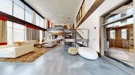Located at 8501 Franklin Square Dr in Baltimore, MD, this impressive two-story clubhouse facility offers a wealth of thoughtfully designed spaces across its two floors. The main level commands attention with soaring double-height ceilings, polished concrete floors, and a dramatic wall of windows that flood the space with natural light. A sleek steel-and-wood cable-railed staircase connects the two levels, complemented by a stylish geometric light fixture overhead.

The main level features an expansive open lounge with contemporary furnishings, a fully equipped kitchen boasting marble countertops, a herringbone tile backsplash, rich wood cabinetry, stainless steel appliances, and pendant lighting. A striking double-sided stone fireplace rises to the full height of the two-story great room, anchoring the space with warmth and architectural grandeur.

The upper level offers additional lounge seating with warm hardwood floors, vibrant orange accent furnishings, and easy access to a private dining room adorned with curated artwork and designer lighting. Additional amenities include a dedicated game room complete with a pool table and bar-height seating, a cozy meeting nook with textured stone walls, and a state-of-the-art media/theater room featuring a large projection screen, sculpted ceiling detail, and bold sectional seating. Throughout, the design reflects a refined, modern aesthetic with rich materials and curated décor.