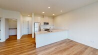 This well-designed one-bedroom, one-bathroom unit at 16017 60th St E in Sumner, Washington offers a thoughtfully arranged single-level layout with modern finishes throughout. Light-toned luxury vinyl plank flooring flows continuously through every room, creating a cohesive and clean aesthetic.

The open-concept kitchen and living area serves as the heart of the unit. The kitchen is outfitted with sleek white cabinetry extending to the ceiling, quartz countertops, stainless steel appliances including a range, built-in microwave, and refrigerator, and a peninsula with an integrated sink that defines the space. Recessed lighting illuminates the living area, which benefits from large windows offering outdoor views and a door providing direct access to a private outdoor deck.

The bedroom is a comfortable, well-proportioned room with a wide window framing neighborhood views and a baseboard heating unit. It connects to a generously sized walk-in closet outfitted with wire shelving along multiple walls, providing substantial storage capacity.

The bathroom features a wide vanity with quartz countertops, ample drawer storage, a large mirror, and a full tub-shower combination. A clean hallway with recessed lighting connects the main living spaces, completing this modern, move-in-ready unit.
