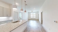 Located at 112 Hera Way in Myrtle Beach, South Carolina, this well-appointed 2-bedroom, 2-bathroom residence offers a thoughtfully designed single-floor layout with a clean, contemporary aesthetic. The open-concept living and kitchen area serves as the heart of the home, where light hardwood flooring, crisp white walls, and abundant natural light from large windows create a bright and airy atmosphere. A ceiling fan anchors the living space, while a private entry door with transom window adds architectural interest.

The kitchen is a standout, featuring a large central island with a granite countertop, undermount sink, and stylish pendant lighting. Grey shaker-style cabinetry, a herringbone tile backsplash, and stainless steel appliances — including a refrigerator, range, and microwave — complete this functional and attractive space.

Both bedrooms are generously sized, finished with plush carpeting and windows that invite natural light and outdoor views. The primary bedroom is notably spacious and includes access to a well-designed en-suite bathroom with a dual-sink granite vanity, hardwood-style flooring, and a walk-in shower. Three closets, including a carpeted walk-in with wire shelving, provide ample storage throughout the residence.