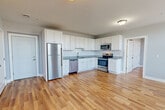 Located at 37 Water Street in Wakefield, MA, this well-designed two-bedroom, two-bathroom residence offers a clean, modern aesthetic across a single floor. The open-concept kitchen and living area serves as the heart of the home, featuring white shaker-style cabinetry extending to the ceiling, granite countertops, a subway tile backsplash, and a full suite of stainless steel appliances including a refrigerator, electric range, microwave, and dishwasher. Warm-toned hardwood flooring flows consistently throughout every room, creating a cohesive and inviting atmosphere. The primary bedroom is a well-proportioned retreat with dual windows that invite natural light, a wall-mounted mini-split HVAC unit for personalized climate control, and direct access to a dedicated closet. The second bedroom also benefits from a bright window and matching hardwood floors. Both bathrooms are finished with neutral tile flooring and tiled tub-shower combinations enclosed by sliding glass doors, offering a clean and functional design. Two closets provide ample storage throughout the residence. The overall palette of soft gray walls, white trim, and light wood tones creates a bright, contemporary living environment.