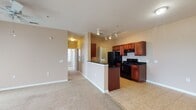 This single-floor residence offers a well-designed layout that balances open communal spaces with private rooms. The living area is generously sized, finished with plush wall-to-wall carpeting, and illuminated by track lighting and a ceiling fan. A large window allows natural light to filter in, enhancing the warm, neutral color palette that flows throughout the unit. The kitchen is defined by rich cherry-toned cabinetry paired with dark granite countertops, black appliances — including a refrigerator, electric range, and built-in microwave — and durable tile flooring. A half-wall peninsula separates the kitchen from the living space, creating an open yet organized flow. In-unit laundry is conveniently accessible directly from the kitchen area. The bedrooms are carpeted and fitted with ceiling fans, and each benefits from natural light provided by windows with blinds. One bedroom features dual windows, offering views of the surrounding area. The bathroom is appointed with a cherry wood vanity, dark granite countertop, an undermount sink, and a shower-tub combination. Throughout the unit, consistent warm beige wall tones and white trim create a cohesive and inviting atmosphere.