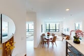 This single-floor residence offers a thoughtfully designed layout that balances open communal areas with comfortable private spaces. The living and dining area serves as the heart of the home, featuring light hardwood flooring, crisp white walls, and recessed lighting throughout. Large grid-style windows with bold black frames flood the space with natural light and offer views of the surrounding neighborhood. The open layout seamlessly connects a dedicated dining space — ideal for a round table and seating — with a relaxed living area anchored by a sofa, coffee table, and additional seating.

The kitchen is outfitted with rich wood cabinetry extending to the ceiling, sleek gray lower cabinets, a gas range, stainless steel appliances including a full-size refrigerator, and clean countertops that make for a functional and stylish cooking space. Two well-proportioned bedrooms provide restful retreats; one features a large picture window with neighborhood views, while the other is a serene primary bedroom with soft, neutral tones. The two bathrooms are finished with large-format tile, one featuring a glass-enclosed walk-in shower and another with a full bathtub, both offering modern vanities and clean, contemporary fixtures.