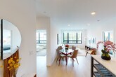 This single-floor residence offers a thoughtfully designed layout that balances open communal areas with comfortable private spaces. The living and dining area serves as the heart of the home, featuring light hardwood flooring, crisp white walls, and recessed lighting throughout. Large grid-style windows with bold black frames flood the space with natural light and offer views of the surrounding neighborhood. The open layout seamlessly connects a dedicated dining space — ideal for a round table and seating — with a relaxed living area anchored by a sofa, coffee table, and additional seating.

The kitchen is outfitted with rich wood cabinetry extending to the ceiling, sleek gray lower cabinets, a gas range, stainless steel appliances including a full-size refrigerator, and clean countertops that make for a functional and stylish cooking space. Two well-proportioned bedrooms provide restful retreats; one features a large picture window with neighborhood views, while the other is a serene primary bedroom with soft, neutral tones. The two bathrooms are finished with large-format tile, one featuring a glass-enclosed walk-in shower and another with a full bathtub, both offering modern vanities and clean, contemporary fixtures.