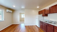 Located at 10500 Hackberry Drive in Sappington, MO, this well-appointed one-bedroom, one-bathroom unit offers a practical and comfortable single-floor layout. The open living and kitchen area is anchored by warm hardwood flooring that extends throughout the main space, creating a cohesive and inviting atmosphere. The kitchen is thoughtfully designed with rich cherry wood cabinetry spanning floor to ceiling, granite-look countertops, a double-basin sink, and a full suite of white appliances including a refrigerator, electric range, and over-the-range microwave. Recessed lighting illuminates the kitchen, adding a clean, modern touch. The bedroom is carpeted for comfort and features neutral, warm-toned walls, a window that invites natural light and outdoor views of the surrounding greenery, and a wall-mounted mini-split HVAC unit for personalized climate control. A closet with a paneled door provides convenient storage. The bathroom is clean and functional, offering a full-size soaking tub and shower combination with chrome fixtures. Throughout the unit, neutral wall tones and white trim create a bright, cohesive aesthetic that is both practical and easy to personalize.