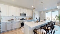 This single-story unit offers a thoughtfully designed open-concept layout that connects the living, dining, and kitchen areas into one cohesive, light-filled space. Light wood-tone flooring runs throughout the main living areas, complementing a neutral, warm color palette on the walls and ceilings.

The kitchen is a standout feature, outfitted with white shaker-style cabinetry, a white subway tile backsplash, quartz countertops, and a full suite of stainless steel appliances including a gas range, microwave, refrigerator, and dishwasher. A central island with seating for two and pendant lighting above adds both functionality and visual appeal.

The living room opens directly to a private balcony through large sliding glass doors, filling the space with natural light and offering views of the surrounding area. Adjacent to the living room, the dining area benefits from an oversized window that further enhances brightness.

The bedroom features carpet flooring and a dedicated closet. Two bathrooms serve the unit, one featuring a tub-shower combination with a vanity and wood-tone flooring. The overall design is clean and modern, with consistent finishes and black hardware details throughout.