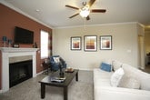 This single-story residence offers a thoughtfully designed layout with warm, neutral tones throughout. The living room serves as a welcoming focal point, featuring crown molding, carpet flooring, a ceiling fan, and a classic fireplace with a tile surround and built-in shelving. Multiple windows with blinds allow natural light to fill the space.

The dining area accommodates a full-sized table and is highlighted by a large window overlooking greenery, complemented by warm accent walls and a pendant light fixture. The kitchen features white cabinetry, dark countertops, black appliances including an electric range and built-in microwave, hardwood-style flooring, and a sliding glass door providing direct access to an outdoor patio.

The bedrooms are carpeted and offer generous proportions, each with a ceiling fan and ample wall space. Two full bathrooms include white vanity cabinetry with dark countertops, large mirrors with overhead lighting, tub-shower combinations, and tile flooring. A dedicated laundry area houses a full-sized side-by-side washer and dryer with overhead shelving for additional storage.