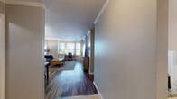 This thoughtfully designed single-floor residence offers a comfortable and functional layout across several well-defined living areas. The living room serves as the centerpiece of the home, highlighted by a striking curved bay window arrangement that floods the space with natural light. Dark hardwood-style flooring runs throughout, complemented by elegant crown molding and neutral-toned walls that create a clean, cohesive aesthetic.

The kitchen is outfitted with white cabinetry, granite countertops, and white appliances, including a range, built-in microwave, and dishwasher. Light wood-style flooring and ample counter space make it a practical and inviting area for cooking. A dedicated in-unit laundry room provides added convenience, housing a full-size side-by-side washer and dryer with wire shelving above.

The bedroom is a tranquil retreat, featuring multiple windows that bring in natural light, a closet with double doors, and direct access to an additional walk-in closet area. The bathroom is generously proportioned, with an extended white vanity, dual sinks, a large mirror with overhead lighting, and tile flooring. Throughout the residence, the consistent use of hardwood-style flooring, crown molding, and neutral tones creates a unified and welcoming atmosphere.
