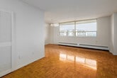 Located on the 9th floor at 2560 Kingston Rd in Toronto's Kingston Road corridor, this one-bedroom, one-bathroom unit offers a practical and well-organized layout. Warm parquet hardwood flooring runs throughout the living areas and bedroom, lending a classic character to the space. The living room is generously proportioned, featuring large floor-to-ceiling windows that flood the room with natural light and provide open outdoor views. A pendant light fixture adds a simple, functional touch to the area, which connects conveniently to the kitchen. The kitchen is finished in white cabinetry with ample upper and lower storage, light-toned countertops, a double sink, and white appliances including a refrigerator and electric range. Light ceramic tile flooring completes the kitchen's clean, bright aesthetic. The bedroom is a comfortable size, featuring its own window for natural light, parquet flooring, a double-door closet for storage, and baseboard heating. The full bathroom is finished in white tile, including a soaker tub with shower, toilet, and vanity with sink. A hallway connects the main spaces efficiently. The unit's bright, neutral palette throughout makes it a versatile and move-in-ready space.
