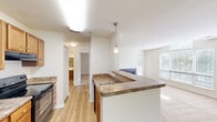 This one-bedroom, one-bathroom unit at 229 Lake Club Court in Charlottesville, Virginia offers a well-organized layout across a single floor. The kitchen serves as a central feature, equipped with warm wood cabinetry, granite-style countertops, black appliances including a refrigerator and electric range, and a peninsula with a built-in sink and pendant lighting overhead. Light hardwood-style flooring runs through the kitchen and entry areas, creating a clean transition into the living space.

The living room is carpeted and benefits from abundant natural light through multiple windows, a ceiling fan, and a set of French doors that open onto a private balcony overlooking lush, wooded surroundings. This outdoor connection adds a sense of openness to the living area.

The bedroom is comfortably sized with soft carpet flooring and direct access to a walk-in closet featuring built-in shelving and hanging rods. The bathroom includes a soaking tub and shower combination with tiled surround and chrome fixtures. In-unit laundry adds everyday convenience. The overall ambiance is bright, neutral, and functional throughout.
