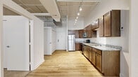 Located in the heart of downtown Cincinnati on West Fourth Street, this one-bedroom unit showcases a distinctive urban loft aesthetic rooted in its building's architectural character. The open-plan living area flows seamlessly from the kitchen toward the living space, unified by light-toned hardwood-style flooring and crisp white walls that maximize the sense of openness. Soaring ceilings with exposed ductwork and industrial-style track lighting reinforce the loft character throughout. The kitchen is well-appointed with rich medium-toned wood cabinetry, granite-look countertops, and a full suite of stainless steel appliances including a range, microwave, dishwasher, and refrigerator. Decorative columns add an architectural accent, hinting at the building's historic bones. The bedroom is carpeted for comfort and features large windows that frame views of the surrounding downtown architecture, filling the room with natural light. Generous closet space is provided via a set of built-in wardrobe closets. The overall ambiance balances industrial character with contemporary finishes, making this a compelling urban retreat in one of Cincinnati's most walkable and vibrant downtown corridors.