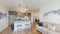 This single-story residence offers a thoughtfully designed floor plan encompassing two bedrooms, three bathrooms, a dedicated office, and an in-unit laundry room. The open-concept living and kitchen area serves as the heart of the home, where warm light wood-style flooring flows seamlessly throughout. The kitchen is outfitted with dark taupe cabinetry, light quartz countertops, a white subway tile backsplash, stainless steel appliances, and a peninsula with bar seating illuminated by pendant lighting. The adjacent living area features a ceiling fan and large windows that invite natural light and outdoor views.

The primary bedroom is a comfortable, well-proportioned retreat with a double-door closet and an en-suite bathroom featuring a tub-shower combination. The second bedroom benefits from multiple windows framing green outdoor views and is served by its own bathroom. A compact but functional office includes a window with exterior views, ideal for remote work. The dedicated laundry room houses a full-sized washer and dryer with overhead shelving. Three bathrooms ensure convenience for residents and guests alike, completing this efficiently organized and modern living space.