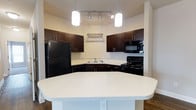 Located at 2030 Wildts Battery Blvd on Johns Island, South Carolina, this single-floor residence offers a thoughtfully designed layout with modern finishes throughout. The kitchen serves as a standout feature, showcasing rich dark espresso cabinetry that contrasts beautifully with light quartz countertops flecked with subtle sparkle. A wraparound peninsula provides generous prep space and casual seating, making it an ideal hub for both cooking and entertaining. Black appliances — including a full-size refrigerator, range, and built-in microwave — lend a sleek, cohesive aesthetic to the space. Overhead, a combination of pendant lights and a track lighting system ensures the kitchen is well-lit and functional. A hanging pot rack adds a practical yet stylish touch above the cook space. The warm-toned walls and hardwood-style flooring visible at the kitchen's edge contribute to an inviting, comfortable ambiance throughout the home. This residence on Johns Island blends modern convenience with a welcoming character, offering a functional and attractive living environment in a growing coastal community just outside of Charleston.