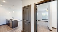 Located at 8310 N Green Hills Rd in Kansas City, MO, this thoughtfully designed one-bedroom, one-bathroom residence offers a clean, contemporary aesthetic across a single floor. The open-concept kitchen and living area serves as the heart of the home, featuring rich dark wood cabinetry, crisp white quartz countertops, a central island with an undermount sink and pendant lighting above, and a full suite of stainless steel appliances including a refrigerator, range, microwave, and dishwasher. Light wood-tone flooring runs throughout the main living areas, complementing the bright white walls and dark trim accents that lend a modern yet inviting character. The living area is bathed in natural light through large windows and is finished with a ceiling fan for added comfort. The bedroom offers plush carpeting, a ceiling fan, and a generous window with outdoor views. The bathroom features dark wood vanity cabinetry, ample drawer storage, and a clean white countertop with a large mirror. Additional spaces include two closets and a utility room, providing practical storage solutions. The overall ambiance is modern and move-in ready, with a cohesive design palette of neutral tones and contemporary fixtures throughout.