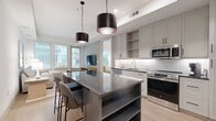 Located at 4604 E Cactus Rd in Phoenix, Arizona, this thoughtfully designed one-bedroom, one-bathroom residence offers a cohesive modern aesthetic across its single floor. The open-concept layout seamlessly connects the kitchen and living area, maximizing the efficient use of space.

The kitchen is a standout feature, showcasing gray shaker-style cabinetry, dark quartz countertops, a white subway tile backsplash with under-cabinet lighting, and a full suite of stainless steel appliances. A central island with a dark quartz surface and built-in shelving provides additional prep space and casual seating beneath two bold cylindrical pendant lights.

The living room is bright and welcoming, with large windows and a glass door that invite abundant natural light and offer outdoor views. Light wood-style flooring runs throughout, contributing to the warm, airy ambiance of the space.

The bedroom is a serene retreat, featuring multiple windows, ample natural light, and two closets for generous storage. The bathroom is elegantly appointed with large-format marble-look tile flooring, a dark gray double vanity with quartz countertops, globe pendant lighting, a framed mirror, and a full tub-shower combination with white subway tile surround.