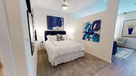 This single-floor residence offers a cohesive and thoughtfully designed interior centered around a refined blue-and-white color palette carried throughout every room. The living area sets an elegant tone with rich navy tufted seating, a glass-top coffee table, hardwood-style flooring, and an ornate sunburst mirror anchoring a mirrored console. Natural light filters through large windows dressed with white curtains, lending the space an airy, welcoming ambiance.

The kitchen is outfitted with crisp white shaker cabinetry, granite-style countertops, stainless steel appliances including an electric range and over-the-range microwave, and a stainless undermount sink — offering both functionality and a clean, modern aesthetic.

The bedroom continues the artistic theme with plush carpeting, a statement navy upholstered headboard, and two bold abstract paintings in vivid shades of blue that bring energy and creativity to the walls. A ceiling fan with a brushed nickel fixture provides comfort overhead, while bedside lamps add warm, layered lighting.

The bathroom features a stone-aggregate countertop with an undermount sink, sleek chrome fixtures, ample mirror space, and carefully selected decorative accents including fresh orchids and framed artwork, completing the space with a spa-like, polished finish.