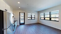 Located at 131 Ionia Ave SW in the heart of downtown Grand Rapids, Michigan, this contemporary single-floor unit offers a clean, modern aesthetic throughout. The open-concept living and dining area is anchored by durable wood-look plank flooring, neutral-toned walls, and black-framed windows that frame views of the surrounding urban cityscape. Recessed lighting and multiple large windows allow generous natural light to fill the space. A private balcony is accessible directly from the main living area, providing an outdoor retreat with city views.

The kitchen is well-appointed with stainless steel appliances — including a refrigerator, electric range, and over-the-range microwave — complemented by white cabinetry, dark granite-style countertops, a tile backsplash, and a stainless steel sink. The layout is efficient and functional, with ample cabinet storage extending to the ceiling.

The bedrooms feature plush carpeted flooring and black-framed windows that bring in natural light and outward-facing city views, creating bright and comfortable retreats. The bathroom is thoughtfully finished with wood-look flooring, a combined tub and shower, a white vanity with dark countertop, and clean white walls. The overall design blends modern urban style with practical, everyday functionality.