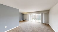 Located at 8587 Greenbelt Rd in Greenbelt, Maryland, this well-appointed single-floor residence offers three bedrooms, two bathrooms, and a thoughtfully laid-out floor plan. The expansive living room is finished with plush wall-to-wall carpeting and neutral-toned walls, creating a bright and welcoming atmosphere. Large sliding glass doors flood the space with natural light and open directly onto a private balcony with outdoor views of the surrounding greenery. The kitchen is efficiently designed with rich dark wood cabinetry, granite-style countertops, light hardwood-style flooring, a skylight panel for added brightness, and a full suite of black appliances including a refrigerator, range, and dishwasher. The primary bedroom is generously sized with soft carpeting and ample natural light, while the additional bedrooms each offer comfortable proportions, carpeted floors, and closet access with built-in shelving. Four closets throughout the residence provide excellent storage capacity. The two bathrooms are clean and functional, one featuring a full tiled tub-shower combination and the other a vanity with overhead lighting. The overall aesthetic is clean, neutral, and move-in ready.