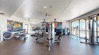 Located at 3510 N Craycroft Rd in Tucson, Arizona, this fitness center offers a thoughtfully designed, single-floor workout space with a generous open layout. The interior is finished with durable dark rubber flooring throughout, recessed ceiling lighting, and ceiling fans that maintain a comfortable environment during workouts.

The facility is comprehensively equipped for both strength and cardiovascular training. A multi-station cable machine serves as the centerpiece, complemented by a dumbbell rack, benches, and an assortment of resistance equipment. Cardio offerings include multiple treadmills, stationary bikes, elliptical trainers, and a stair climber. A dedicated stretch and functional training area features stability balls, foam rollers, and a water station.

One of the most distinctive design elements is the large-scale desert landscape wall murals, depicting iconic Sonoran Desert scenes — including saguaro cacti, mountain vistas, and vivid Arizona sunsets — creating an immersive, regionally inspired atmosphere. Floor-to-ceiling windows and sliding glass doors along one wall flood the space with natural light and provide sweeping views of the surrounding Tucson landscape. The combination of vibrant artwork, natural light, and high-quality equipment makes this fitness center both functional and visually engaging.