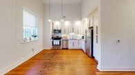 Located at 2110 Pickens St. in Columbia, South Carolina, this single-floor residence blends classic architectural character with thoughtful modern updates. Rich hardwood floors run throughout the main living and bedroom areas, complementing the crisp white walls and tall ceilings that lend the space an open, airy feel.

The kitchen is a standout feature, showcasing white shaker cabinetry with matte black hardware, granite countertops, a white subway tile backsplash, and a full suite of stainless steel appliances including a range, microwave, dishwasher, and refrigerator. Pendant lighting and generous natural light from a nearby window enhance the bright, functional workspace.

The living area offers a welcoming atmosphere with large windows dressed with decorative ironwork grilles, warm hardwood floors, and built-in niche shelving that adds architectural interest. Multiple bedrooms are well-proportioned and finished in neutral tones with hardwood flooring, providing comfortable, versatile spaces.

The bathrooms are finished with tile flooring, granite-topped vanities with dark cabinetry, and tub/shower combinations with curved curtain rods. Additional rooms include a flexible space with concrete flooring and ample closet storage, including a set of double doors offering generous capacity. The overall ambiance is clean, classic, and move-in ready.