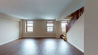 This two-floor residence offers a well-organized layout with distinct living spaces distributed across both levels. The main floor features an open living area with rich hardwood-style flooring that extends throughout, neutral-toned walls, and multiple windows fitted with dark-trimmed frames that bring in natural light. A staircase with a warm wood balustrade and newel post connects the two floors, serving as a functional architectural focal point in the living space.

The kitchen is outfitted with white shaker-style cabinetry, granite-look countertops, and a full suite of stainless steel appliances including a refrigerator, electric range, built-in microwave, and dishwasher. Light tile flooring completes the kitchen's clean, practical aesthetic.

The upper level hosts carpeted bedrooms finished in soft, neutral tones. Each room is generously proportioned with windows providing natural light and ample wall space. Two bathrooms serve the unit: one features a tiled tub-shower combination with light stone-look tile and tile flooring, while the second includes a white vanity with a large mirror and tile floors, offering a clean, functional design throughout.