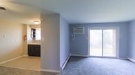 This single-floor space offers a clean, functional layout designed for comfortable everyday living. The living area is finished with plush carpeting and painted in soft, neutral tones that create a calm and airy atmosphere. A wall-mounted air conditioning unit and baseboard heating ensure year-round climate comfort. A sliding glass door floods the space with natural light and provides direct access to a private balcony, offering a pleasant outdoor retreat.

Adjacent to the living area, the kitchen is separated by a partial wall that maintains an open and connected feel. The kitchen features dark cabinetry that contrasts beautifully with a classic tile backsplash, providing a stylish and practical cooking environment. A single-basin sink is positioned beneath a window, allowing natural light to brighten the workspace. The kitchen floor is finished with neutral tile, offering easy maintenance and a clean aesthetic.

Throughout the space, the consistent color palette and thoughtful design choices contribute to a cohesive and welcoming environment. The combination of carpeted living areas, tiled kitchen, and access to outdoor space makes this a well-rounded and practical single-floor residence.
