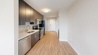 Located in Alexandria, Virginia, this thoughtfully designed one-bedroom, one-bathroom residence offers a modern aesthetic throughout its efficient, single-floor layout. Light-toned hardwood-style flooring extends through the main living areas, creating a clean and cohesive look.

The galley-style kitchen is a standout feature, outfitted with dark wood cabinetry, a tiled backsplash, white quartz countertops, and a full suite of stainless steel appliances including a refrigerator, electric range, microwave, and dishwasher. The kitchen flows naturally toward a bright living area, which benefits from natural light through a large window with views of the surrounding Alexandria neighborhood.

The bedroom is carpeted for comfort and features a sliding closet with built-in hanging rods, as well as a window that brings in additional natural light. The neutral, warm-toned walls provide a calm and restful atmosphere.

The bathroom is finished with large-format tile flooring, a tiled tub-shower combination with a curved curtain rod, a vanity with a white countertop and wood-tone cabinetry, and chrome grab bars for added accessibility.

A dedicated laundry area houses a stacked washer and dryer unit, adding significant everyday convenience. Clean lines, neutral tones, and modern finishes throughout give this residence a polished, contemporary character.