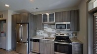 Located at 200 E Six Forks Rd in Raleigh, NC, this single-floor space showcases a modern design aesthetic with thoughtfully selected finishes throughout. The kitchen stands out as a highlight of the space, featuring a cohesive color palette built around dark wood-grain cabinetry that extends floor to ceiling, providing generous storage. Upper cabinets include glass-front panels, adding visual depth and a refined touch to the overall design.

The countertops are finished in speckled granite, offering both durability and style, while a stainless steel under-mount sink adds a clean, contemporary look. A geometric mosaic tile backsplash in neutral tones of white and gray creates a dynamic focal point behind the range, tying together the kitchen's modern aesthetic.

The kitchen is fully equipped with a complete suite of stainless steel appliances, including a French door refrigerator, electric range with oven, over-the-range microwave, and dishwasher. The cabinetry hardware features sleek bar-style pulls that complement the overall modern design. Recessed lighting and neutral wall tones complete the space, creating a bright and functional environment well-suited for everyday living.
