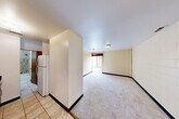 Located at 121 E Hoover Ave in Ann Arbor, MI, this one-bedroom, one-bathroom unit offers a practical and efficient single-floor layout. The combined living and dining area forms the heart of the space, featuring neutral-toned painted cinder block walls, light carpeting, and a window that allows natural light to filter in. The kitchen is separated by a partial wall partition and features tile flooring, wood cabinetry, and includes a full-size refrigerator, providing functional cooking and storage space. The spacious primary bedroom is carpeted with neutral walls and includes a mirrored sliding-door closet, offering ample storage. A second closet is accessible from the main living area, also with mirrored sliding doors. The bathroom features a warm wood vanity with a dark granite countertop, an undermount sink, and a large mirror. A dedicated utility room provides additional in-unit convenience. The entrance transitions between the tiled kitchen area and the carpeted living space, with warm wood-trimmed doors throughout adding a cohesive design element. The unit's straightforward layout and practical features make it a well-organized and functional living space.