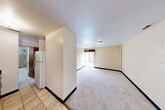 Located at 121 E Hoover Ave in Ann Arbor, MI, this one-bedroom, one-bathroom unit offers a practical and efficient single-floor layout. The combined living and dining area forms the heart of the space, featuring neutral-toned painted cinder block walls, light carpeting, and a window that allows natural light to filter in. The kitchen is separated by a partial wall partition and features tile flooring, wood cabinetry, and includes a full-size refrigerator, providing functional cooking and storage space. The spacious primary bedroom is carpeted with neutral walls and includes a mirrored sliding-door closet, offering ample storage. A second closet is accessible from the main living area, also with mirrored sliding doors. The bathroom features a warm wood vanity with a dark granite countertop, an undermount sink, and a large mirror. A dedicated utility room provides additional in-unit convenience. The entrance transitions between the tiled kitchen area and the carpeted living space, with warm wood-trimmed doors throughout adding a cohesive design element. The unit's straightforward layout and practical features make it a well-organized and functional living space.