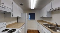 Located at 10615 Abercorn St in Savannah, Georgia, this two-floor residential space offers a practical and well-organized layout suited for comfortable everyday living. The galley-style kitchen is a standout feature, designed for efficient use of space with white cabinetry lining both sides from floor to ceiling, providing generous storage throughout. Light-toned countertops offer ample workspace, while white appliances — including a refrigerator and electric range — lend the kitchen a clean, cohesive aesthetic. Warm hardwood flooring runs the length of the kitchen, adding a touch of character and contrast to the bright white cabinetry. A small window at the far end of the kitchen allows for natural light to filter in, enhancing the sense of openness within the galley layout. Overhead fluorescent lighting ensures the kitchen remains well-lit at all times. The two-floor configuration of the overall space suggests a thoughtful separation of living and private areas, a common feature that supports both functionality and comfort. The overall design reflects a straightforward, practical approach to residential living in the heart of Savannah.