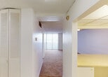 Located at 1400 NW Tenth Avenue in Miami's Health District, this single-floor unit offers a straightforward, functional layout suited to everyday living. The interior is organized around a central hallway that connects the main living spaces, with a louvered closet providing built-in storage near the entry. The textured ceilings are consistent throughout, contributing to the unit's classic character.

The living area is generously proportioned, finished with wall-to-wall carpeting in a warm neutral tone and illuminated by a ceiling fan with integrated lighting. A full-width sliding glass door fitted with vertical blinds opens to an outdoor view of the surrounding Miami skyline, allowing natural light to fill the space. An adjacent carpeted area, similarly bright and open, connects seamlessly to the rest of the unit.

The kitchen features tile flooring and a pass-through counter that connects to the living space, creating an open, accessible feel. The bathroom is finished with distinctive small-scale mosaic tile work lining the tub surround and lower walls, complemented by a white vanity, a large mirror, and overhead lighting. The tile flooring continues the cohesive aesthetic throughout the wet areas of the unit.