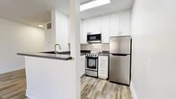 Located at 2235 W Broadway in Anaheim, CA, this single-floor unit makes smart use of its compact footprint with a thoughtful, open-concept layout. The combined living, dining, and kitchen area forms the heart of the space, unified by wood-look plank flooring and crisp white walls that lend a clean, modern aesthetic throughout. A ceiling fan with integrated lighting anchors the living area, which opens directly to a private patio through a sliding glass door, allowing natural light to fill the room and providing a pleasant outdoor extension of the living space. The kitchen is well-appointed with white shaker cabinetry, dark countertops, a subway tile backsplash, and a full suite of stainless steel appliances including a range, microwave, and refrigerator. A skylight above the kitchen adds an additional source of natural light, brightening the workspace. A pass-through counter connects the kitchen to the dining and living areas, enhancing the open flow. The unit includes two bathrooms, one featuring a tub-shower combination with clean white surrounds. A dedicated closet provides practical storage, while the consistently applied wood-look flooring ties all areas together for a cohesive, contemporary feel.