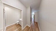Located at 1100 Broadway Street in Ann Arbor, Michigan, this efficiently designed studio unit offers a thoughtful single-floor layout that maximizes every square foot. The open-concept kitchen and living area serve as the heart of the space, featuring warm hardwood-style flooring throughout. The modern kitchen is outfitted with a full suite of stainless steel appliances — including a gas range, over-the-range microwave, dishwasher, and refrigerator with ice maker — complemented by two-tone cabinetry with white upper cabinets and light wood lower cabinets, a white quartz countertop, and a sleek subway tile backsplash. The living area is highlighted by a Murphy bed unit integrated with a sofa, maximizing functionality, along with a large floor-to-ceiling window that floods the space with natural light and provides views of the surrounding neighborhood. A hallway connects the main living area to the full bathroom, which includes a glass-enclosed walk-in shower, a white vanity with under-sink storage, and consistent hardwood-style flooring. A dedicated closet provides additional storage. The unit features neutral gray walls and crisp white trim throughout, creating a clean, contemporary aesthetic well-suited for modern urban living.