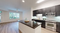 Located at 3443 Kingsboro Rd NE in Atlanta's vibrant Buckhead neighborhood, this single-floor residence offers a clean, contemporary design with thoughtful finishes throughout. The open-concept layout connects the kitchen and living area seamlessly, creating a bright and airy atmosphere enhanced by natural light from large windows that frame lush greenery outside.

The kitchen is a standout feature, outfitted with dark espresso cabinetry, rich dark granite countertops on both the island and perimeter, a classic tile backsplash with under-cabinet lighting, and a full suite of stainless steel appliances including a gas range, built-in microwave, dishwasher, and refrigerator. The oversized kitchen island provides generous prep and serving space.

Light-toned hardwood floors extend throughout the main living areas and bedrooms, complemented by crisp white walls and elegant crown molding that add a polished architectural detail to every room. A ceiling fan in the living area enhances comfort. The bedroom is well-proportioned, offering access to a private en-suite bathroom featuring large-format tile flooring, a dual-sink vanity with dark cabinetry, a wide mirror, and recessed lighting. An in-unit washer is also conveniently located within the bathroom corridor, adding everyday practicality to this well-appointed home.